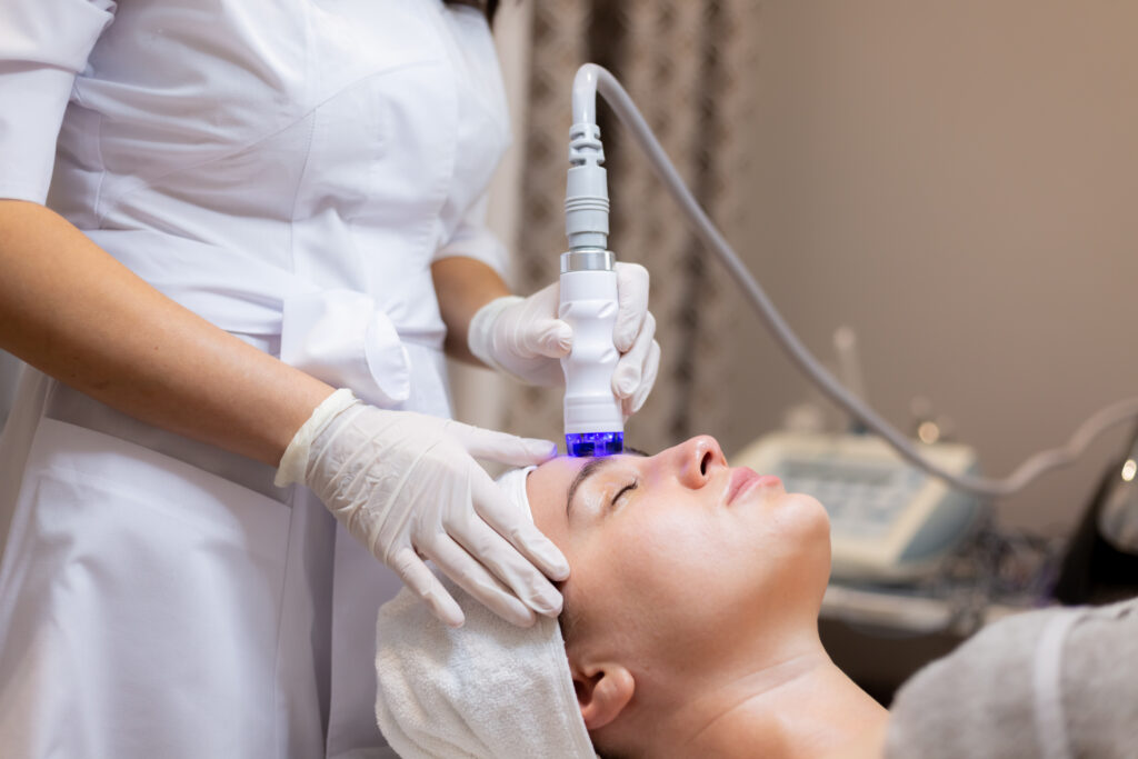 A young beautiful girl lies on the beautician's table and receives procedures with a professional apparatus for skin rejuvenation and moisturizing