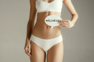 Woman health. Female model holding card near stomach. Young adult girl with paper with word WELLNESS isolated on gray studio background.