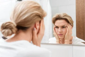 Woman looking into mirror frustrated from migraines