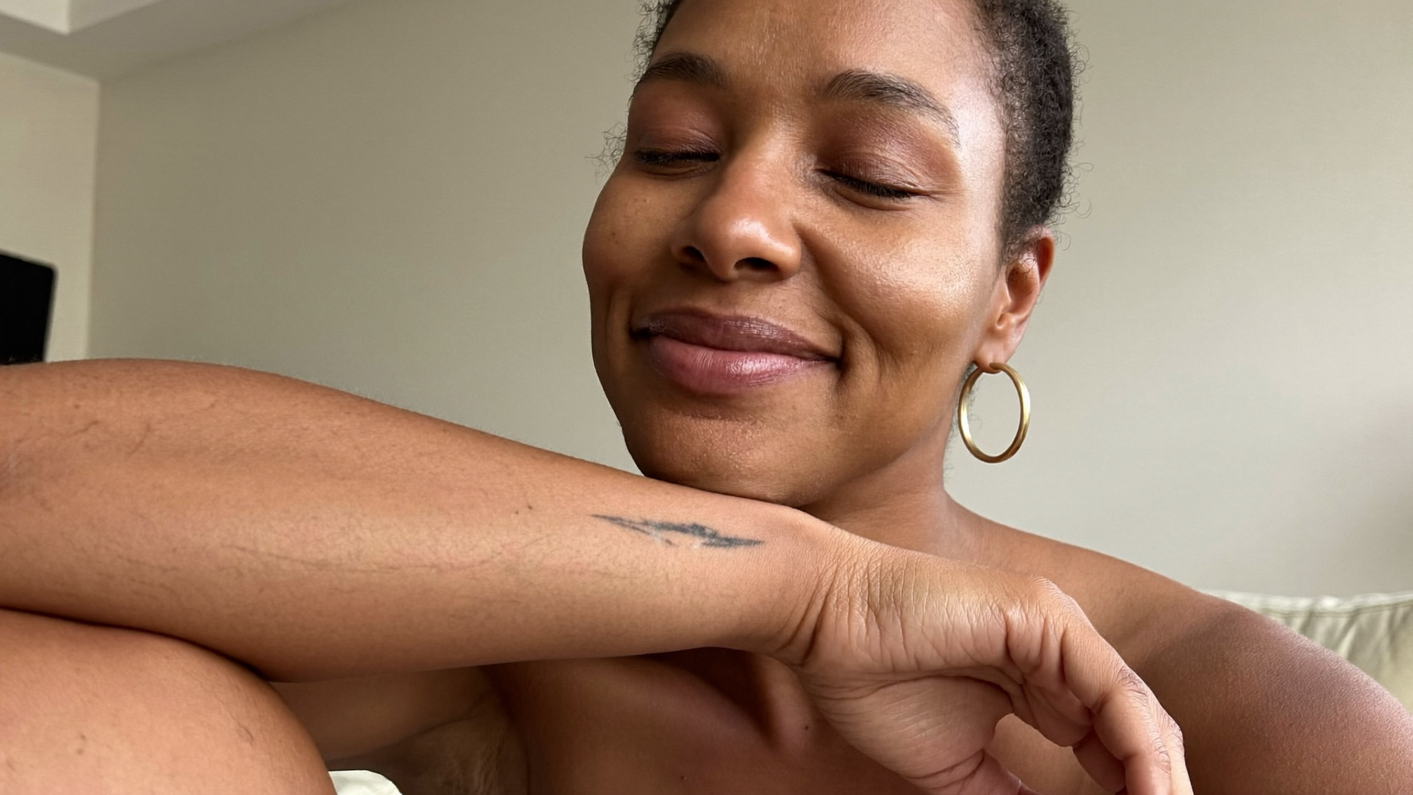 Adult woman with a relaxed expression touching her smooth forearm in soft natural light, representing lasting laser hair removal results