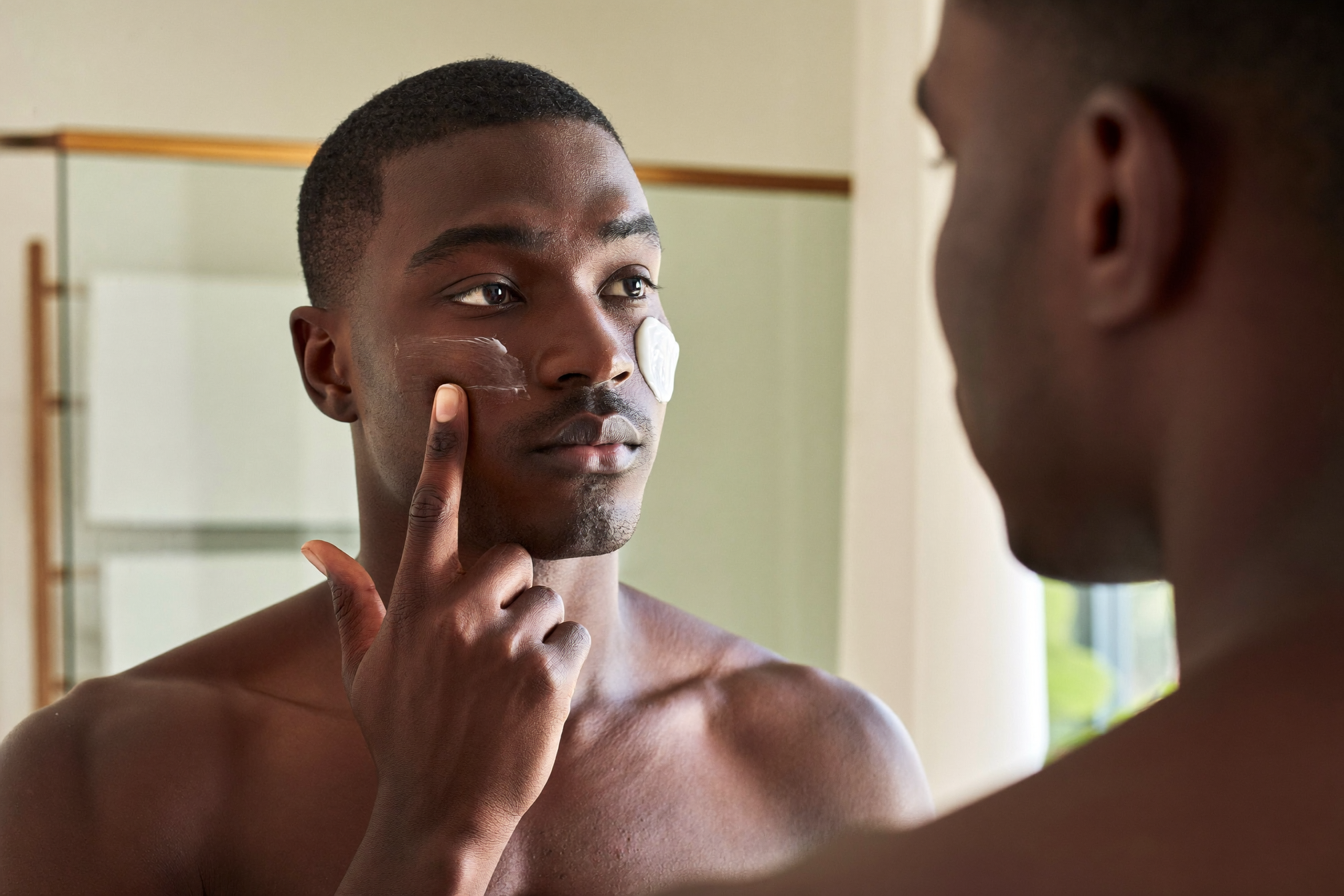 Adult man with deep skin tone applying moisturizer to renewed, glowing skin after a peel